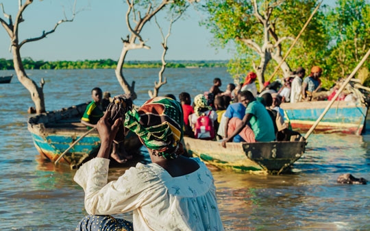 Woman giving her back to the camera and looking at a group of boys going boating