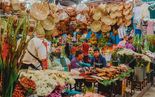 Two people chatting behind a stand with hats and fruits