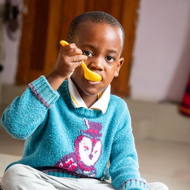 A child eating porridge with a yellow spoon